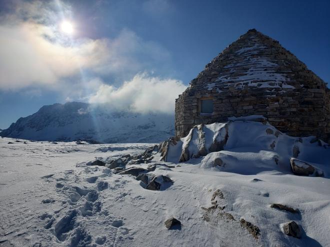 A charming stone building in a snowy landscape, with sunlight streaming down from a clear sky above.